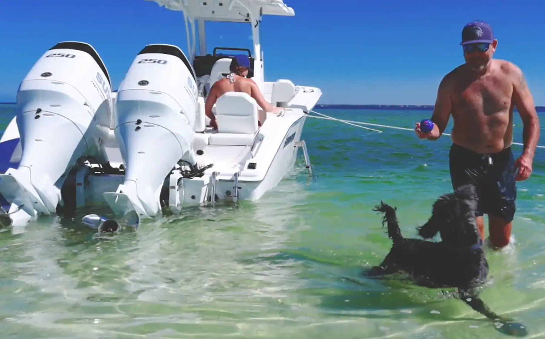 A family and their dog wading beside a twin-outboard boat on a Gulf Coast sandbar